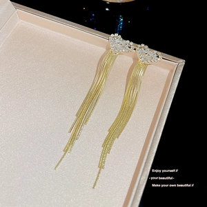 Close-up of golden heart drop earrings with tassels on a jewelry box background