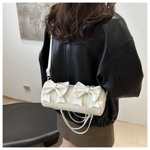 White cylinder crossbody bag with double bow details worn over a black leather jacket