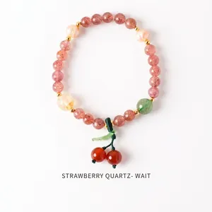 Close-up of strawberry quartz beaded bracelet with a cute cherry charm and golden accents