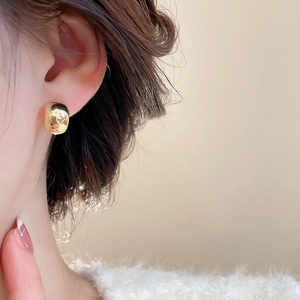 Detailed view of elegant gold C-shaped pearl earrings worn with a cozy knit sweater