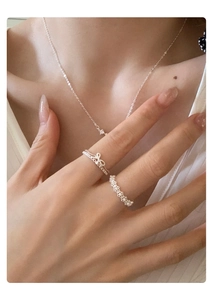 Close-up of bow ring, lace band and zircon necklace worn by a model in silver