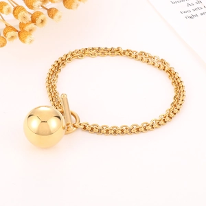 Detailed shot of a gold chunky double-chain bracelet with a large ball pendant and toggle clasp