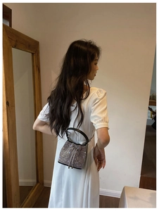 Silver rhinestone bucket bag with black handle shown on model wearing a white dress