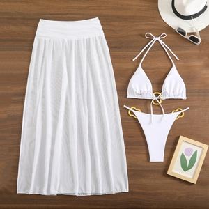 Detailed flat lay of white three-piece bikini set with gold rings and mesh skirt on wood