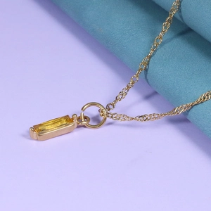 Close-up of golden necklace with rectangular yellow zircon pendant on fabric