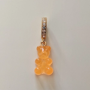 Macro detail of an orange gummy bear resin pendant with gold zircon-studded clasp
