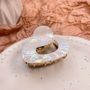 Close-up of heart-shaped white acetate hair claw clip with golden metal teeth