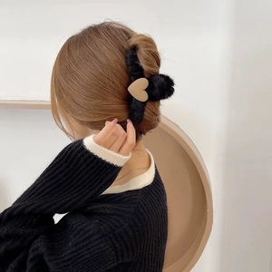 Detail of soft black plush claw clip with beige heart accent worn on model's hair