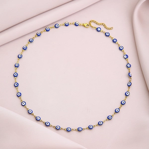 Flat lay of gold tone evil eye chain necklace with blue and white beads on pink fabric