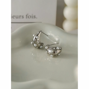 Macro shot of silver C-shaped earrings with white pearls and sparkling rhinestones