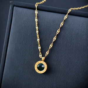 Macro view of gold pendant featuring a green faceted gemstone with Roman numeral engraving