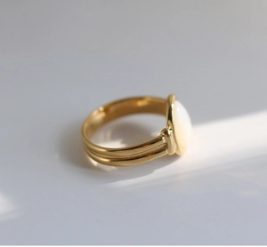 Macro view of gold split-shank ring featuring a white oval mother-of-pearl gemstone