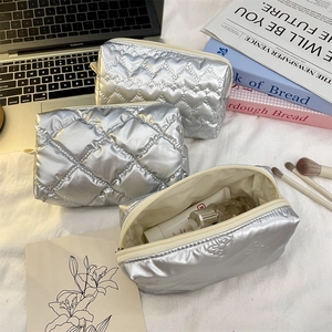 Detailed view of silver quilted makeup bags with heart and diamond patterns on white fabric