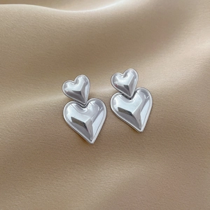 Close-up of double heart titanium steel stud earrings on beige silk fabric background