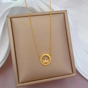 Detail of gold crown pendant necklace engraved with LUCKY on beige jewelry box with silk
