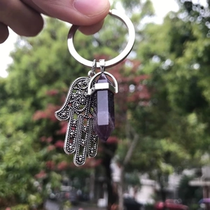 Detail showing a silver Hamsa hand charm and a purple amethyst crystal pillar on the keychain