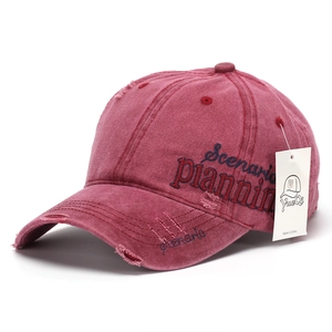 Detail of side embroidery on distressed burgundy baseball cap with brand tag