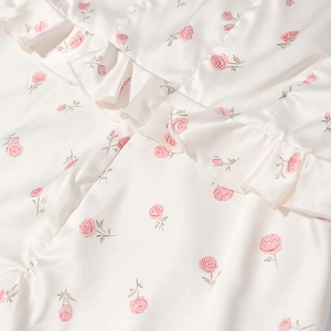 Vue détaillée du motif floral de roses roses sur tissu satiné blanc soyeux avec volants