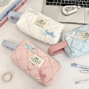 Quilted glossy pouches in white, pink, and blue with bow details on a desk setting