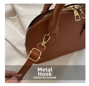 Close-up of golden metal hooks and brown crocodile texture on a shell-shaped bag