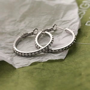 Orecchini a cerchio in argento con texture a perline e marchio S925 su sfondo verde