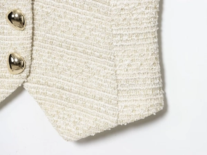 Gros plan sur la texture du tweed beige avec des boutons dorés sur le gilet chic