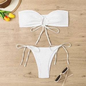 Flat lay of white bandeau bikini set with textured fabric and side-tie bottom on wood