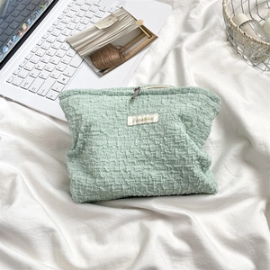 Detail of mint green textured makeup bag with soft pleated fabric and silver zipper