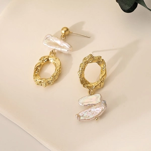 Asymmetric gold earrings with baroque pearls and hammered texture on beige plate