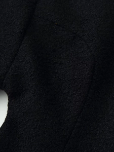 Close-up of black curly wool fabric texture on a wide-cut winter wool coat for women