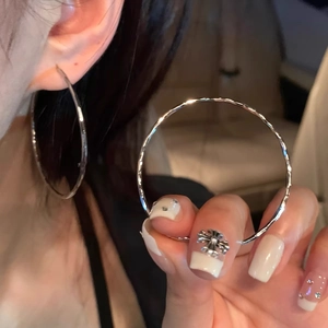 Détail d'une grande boucle d'oreille créole en argent portée à l'oreille au design épuré