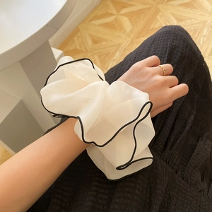 Close-up of beige chiffon scrunchie with black trim worn on a model's wrist