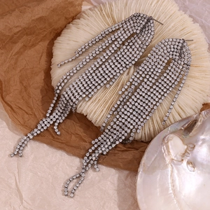 Macro detail of long silver fringe earrings with multi-row pave rhinestones on white texture