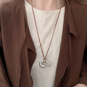 Irregular C-shaped metallic pendant necklace on brown cord worn over elegant clothing