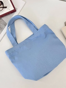 Blue canvas tote bag with double handles shown on desk with lifestyle accessories