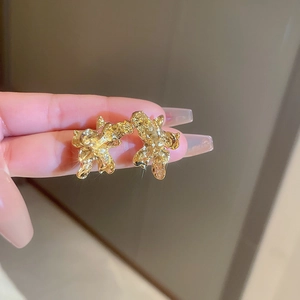 Close-up of golden irregular lava texture metal earrings with glossy reflective finish