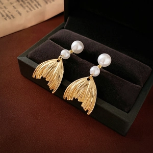 Detail shot of golden fishtail pearl earrings displayed in a luxury dark velvet jewelry box