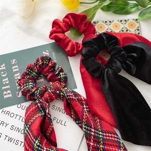 Close-up of velvet and plaid Christmas hair scrunchies with long ribbons on white fabric
