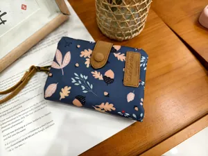 Detail of navy blue trifold wallet with autumn maple leaf pattern and brown leather strap