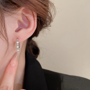 Close-up of elegant silver C-shape earrings with small pearls worn on a model's ear
