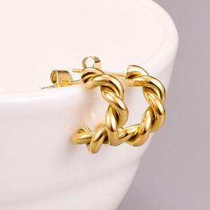 Macro view of golden twisted hoop earrings resting on white ceramic edge for jewelry detail