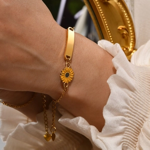 Close-up of gold sunflower charm bracelet with rectangular custom nameplate for women