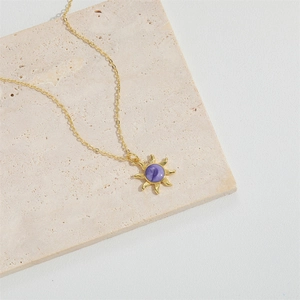 Golden sun pendant necklace with purple center stone displayed on a beige stone block