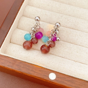 Detail of opal tassel earrings with colorful beads and silver needle studs on beige base
