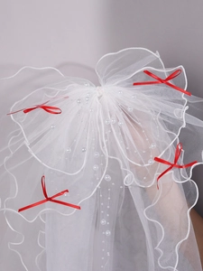 Detail of white bridal veil with multiple mesh layers, pearls, and red decorative bows