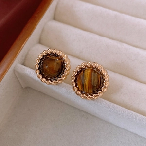 Detail of round tiger eye earrings with golden twisted rope borders in a white jewelry box