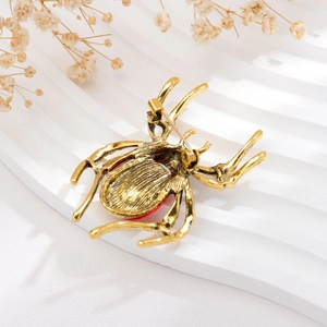 Detailed back view of golden spider brooch with a red gemstone on textured surface