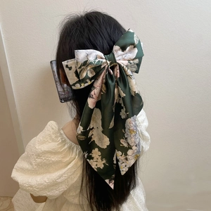 Detailed view of dark green satin bow hair clip with elegant floral pattern on model