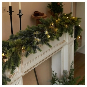 Close-up of artificial pine garland with warm LED lights on a white fireplace mantel