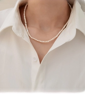 Close-up of minimalist natural white pearl necklace worn on a white collared shirt